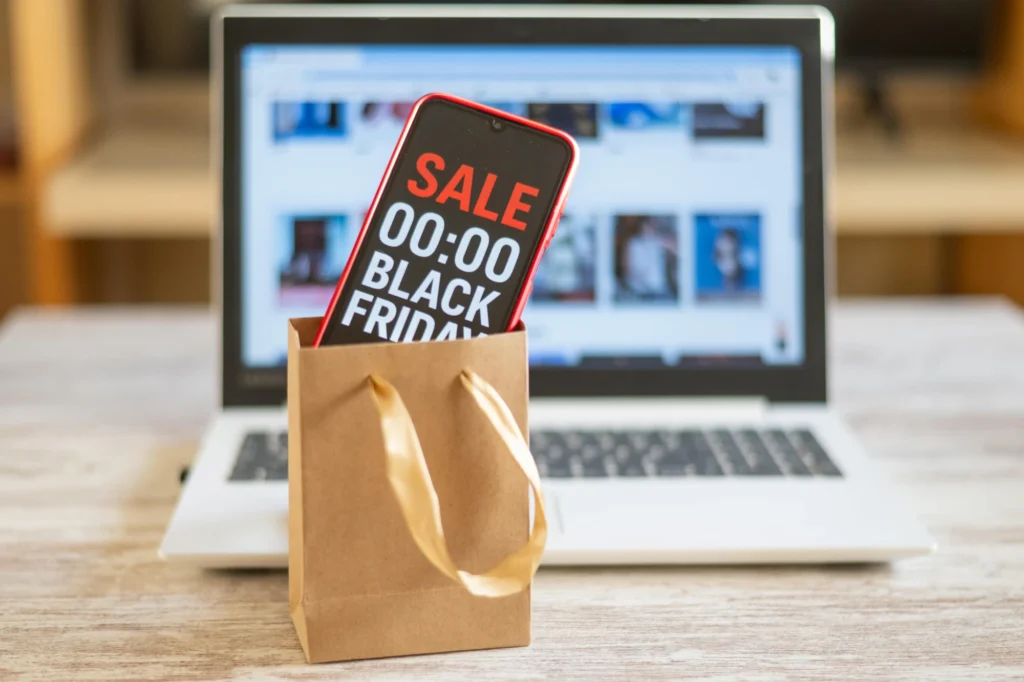 Smartphone con la scritta Sale Black Friday in un sacchetto regalo davanti a un portatile